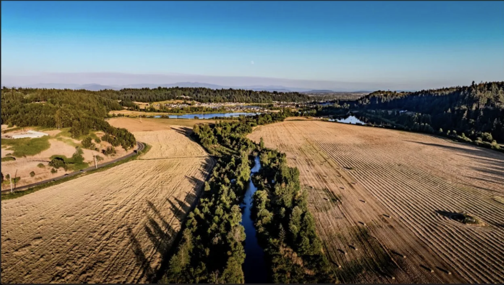 Aerial view of the Herren Crossing property — Mill Creek winding through harvested agricultural fields, Cascade foothills in the distance